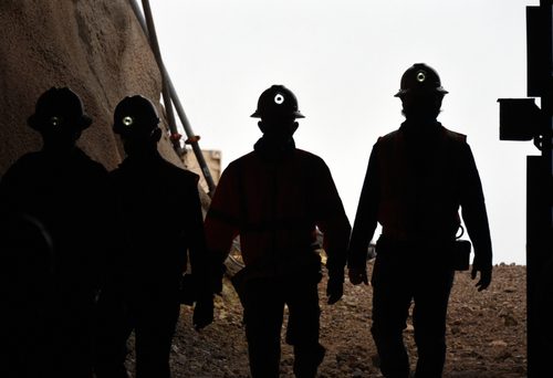 Outline of team of miners wearing helmets walking in a mine